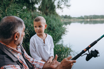 grandfather teaching his grandson how to fish outdoor on the lake