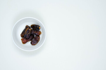 Dates or kurma in white ceramic bowl on white background. Copy space
