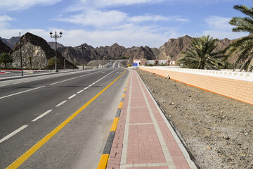 Fototapeta premium Well conserved Al Saidiya Street lined by mountains and palm trees, close to Muscat, Oman.