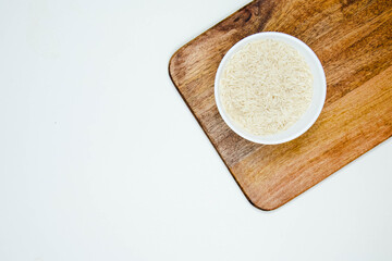 Bowl of long grain white rice, on black walnut chopping board isolated on white background. Copy space