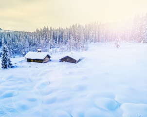 Idyllic mountain log cabin covered in deep snow in a scenic winter sunset in the wild.