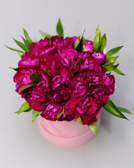 Round flower composition of pink flowers in cylindrical gift box. Top view of red roses, flat lay. Bright fuchsia bouquet on grey background. Valentines day present.