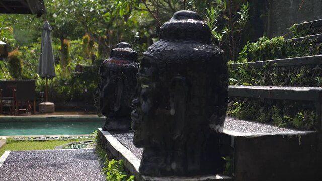 Close up of balinese head figures staying in the rain next to the swimming pool