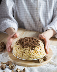 Traditional russian anthill cake in female hands on a wooden board. Soviet sweets. Vertical orientation, selective focus