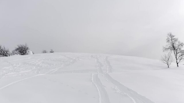 Aerial view of snowy mountain peak with ski tracks on snow in a winter and foggy journey. Some trees on side