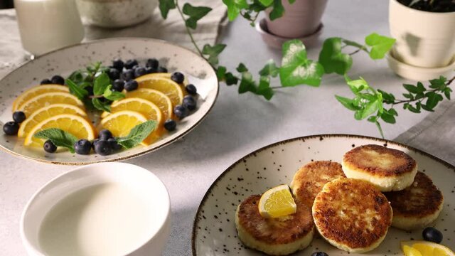Delicious breakfast with curd fritter or cottage cheese pancakes on plate. Camera moving along table surface. Sunny morning light.