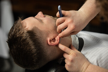 Close up hands of master barber, stylist with razor does the hairstyle to guy, young man. Professional occupation, male beauty concept. Cares of hair of client. Soft colors and focus, vintage.