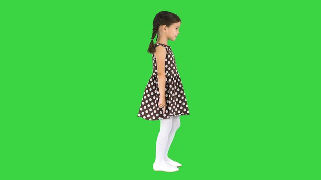 Little girl in polka dot dress dancing and raising her arms on a Green Screen, Chroma Key.