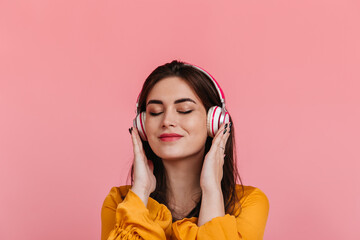 Portrait of satisfied girl without makeup in headphones on pink background. Model smiling while listening to pleasant melody