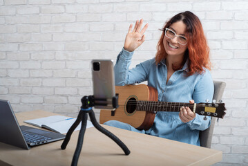 Caucasian woman playing guitar live on a smartphone. The girl leads a music video blog