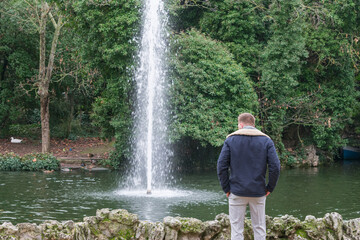 young man sitting contemplating a lake water fountain