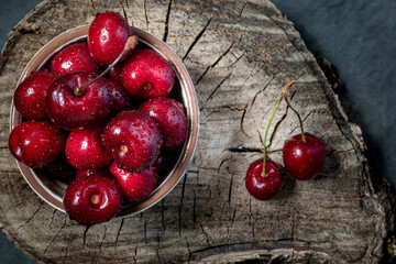 Many large ripe cherries are covered with water drops. Sweet berries on a wooden slice.