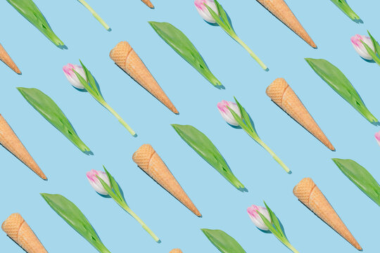 Creative spring pattern made with ice cream cones, pink tulips and green leaves on blue background.