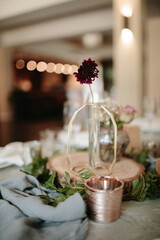 Vintage wedding decor. Beautiful event venue. Creative decoration. Hall decoration. Festive table decor. Stylish stone tablet with table number in grey, green branches and peonies, candles in gold can