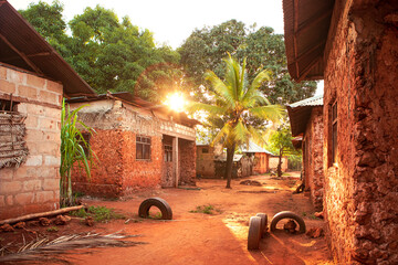 Scenic sunset over african village with palm. Street full of light, vibrant red soil and red color...