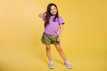 beautiful little girl in a purple t-shirt and shorts posing on a yellow background. A cute baby. Photo in studio