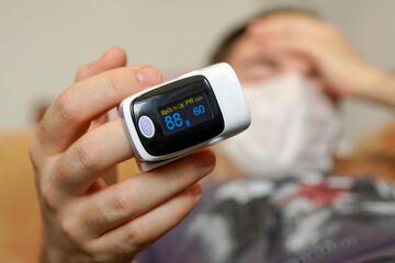 young man is sick with COVID-19 coronavirus and measures oxygen saturation at home on the couch. Pulse Oximeter portable digital device Covid-19 viral pneumonia. Selective focus.