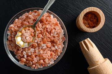 Glass bowl of himalayan salt with small spoon and wooden salt mill on black background