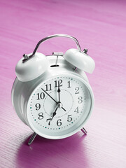 White clock alarm clock showing seven o'clock on purple background vertical shot