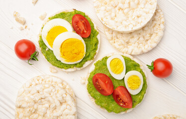 Top view rice cakes with avocado mash and eggs with tomato on wooden background