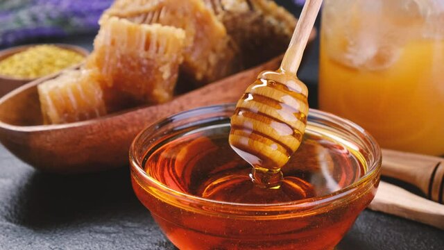 Honey in glass jar with honey dipper over wooden background with honeycomb and propolis, liquid sugar syrup, flower nectar