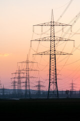Electricity pylons and electric power transmission lines against vibrant orange sky at sunset. High...
