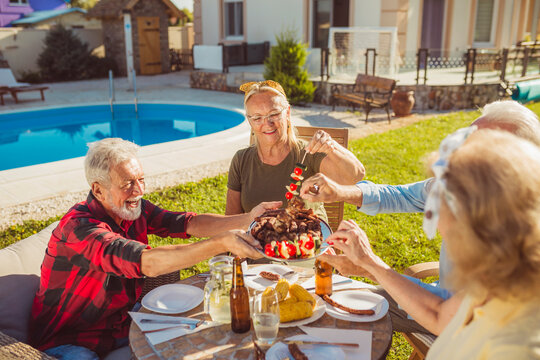Elderly man serving food on a tray while having lunch with friends in the backyard