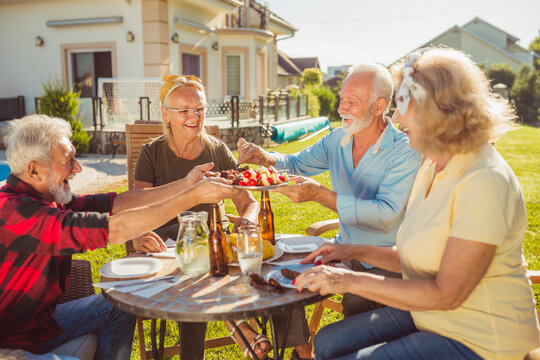 Elderly man serving food on a tray while having lunch with friends in the backyard