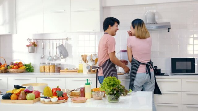 Happy asian couple making health food in kitchen room at home. Young couple make fun and tease while preparing healthy food together indoors. Husband and wife prepare vegetable and fruit for salad.