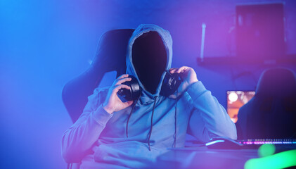 incognito hacker professional cyber gamer playing online computer game with headphones, Blurred Red and Blue background © Parilov