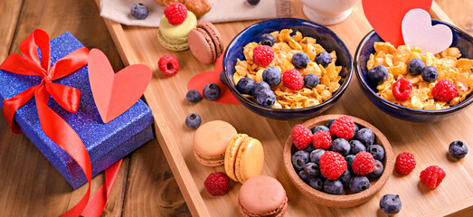 Obraz na płótnie Canvas Sweet surprise, gift in Valentine's Day. Breakfast for a couple of lovers. Aromatic coffee, muesli with berries and sweet pastries on a wooden table. Above. High quality photo
