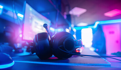 Professional headphones with microphone for video games and cyber sports gaming monitor in neon color blur background - obrazy, fototapety, plakaty