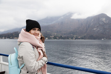 Passage cruise woman tourist in fjords Scandinavian countries. Dressed in hat, scarf and backpack. Looks into distance mountains in fog