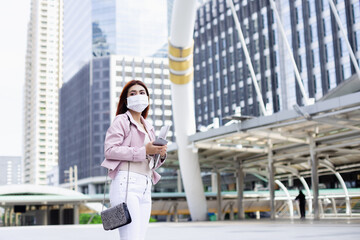 Asian women red hair wearing medical face mask for prevent dust and protect coronavirus pandemic, standing in business city center.