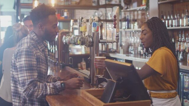 Male customer in bar paying bartender for drink using contactless card and social distancing during health pandemic - shot in slow motion