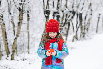 Happy cute little kid use smart phone funny face mask app look at cell screen smiles at something funny. Holidays and celebrations concept. Outside. The dead of winter, cold weather, frost, snow.