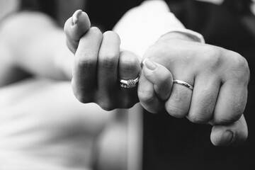 photo of wedding rings on the hands of the newlyweds in grayscale color. Background blurred for...