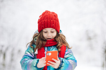 Happy little kid use smart phone funny face mask app look at cell screen smiles at something funny. Holidays and celebrations concept. The dead of winter, cold weather, frost, snow.