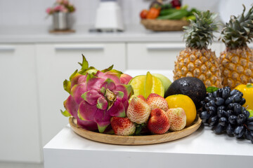 Grapes, dragon fruit, strawberry, pineapple, orange, many fruits in a wooden tray on the kitchen table.