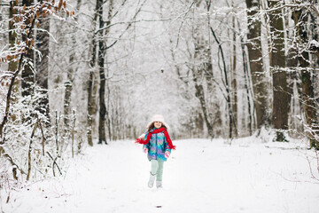 Happy child girl plays with a snow in winter day. Girl enjoys winter, frosty day. Cute little happy girl in winter clothes is having fun running in snowy winter day
