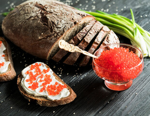 Red caviar and bread with butter on a black background