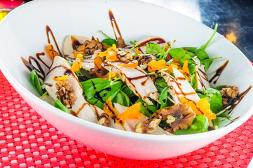 Fresh salad with chicken breast, arugula, nuts on black plate in a wooden table.