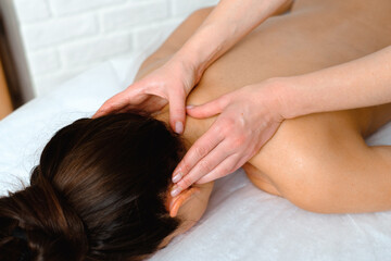 Close-up of a beautiful Caucasian woman getting a head and neck massage at a spa. A woman lies on a massage table on a white brick background