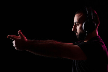 Bearded young Arab DJ musician listens music with headphones and depicts gun with his hands. International DJ Day