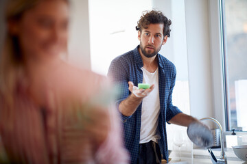 A young guy asking his girlfriend to help him with washing the dishes. Kitchen, relationship,...