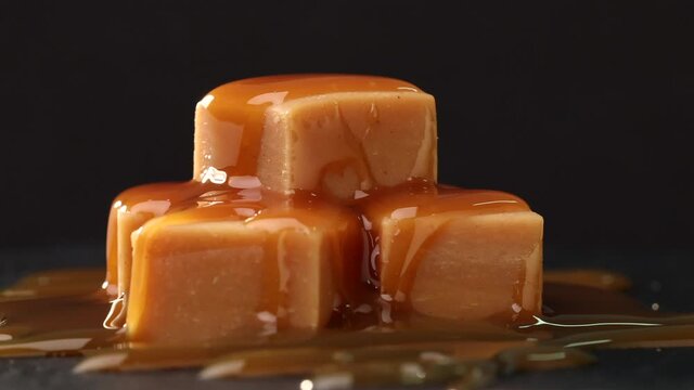 rotating caramel candies covered with melted caramel sauce close up on black background