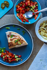 Fresh gluten free tortilla wrap on a plate stuffed with chickpea falafel, fresh vegetables chopped salad, fried onion rings, jalapenos, mayo and scallions. Healthy tasty meal preparation. Top view.