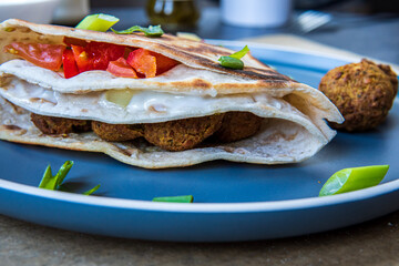 Fresh gluten free tortilla wrap stuffed with chickpea falafel, fresh vegetables chopped salad, fried onion rings, jalapenos, mayo and scallions. Healthy and tasty meal preparation. Side view.