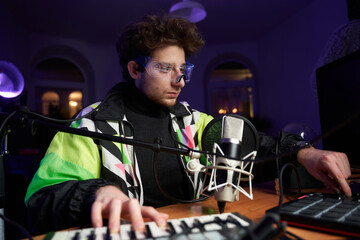 Young composer making a music with modern musical equipment a Midi keyboard a Drum pad and a Microphone in dark room.