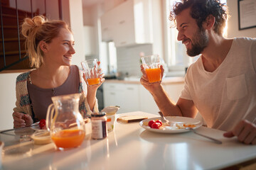 A happy young couple drinking a fresh orange juice after breakfast. Relationship, love, together,...